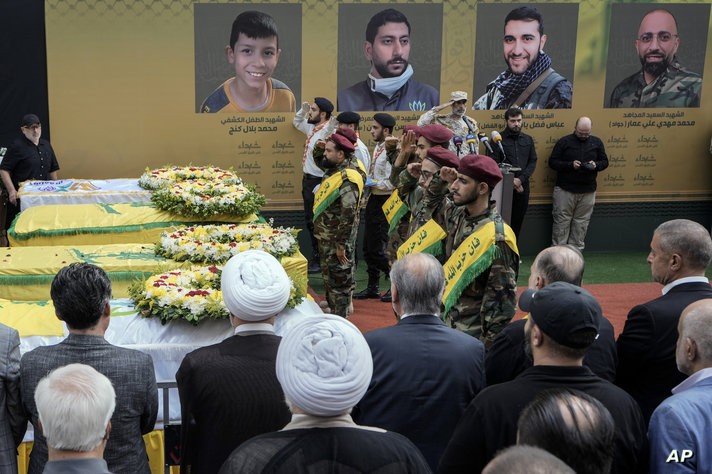 Hezbollah fighters salute as they stand next to the coffins of four victims who were killed Tuesday after their handheld pagers…