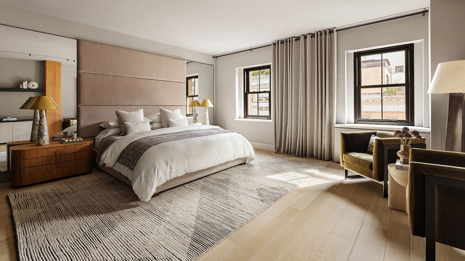 تتميز غرفة النوم الرئيسية بأرضيات خشبية فاتحة اللون ونوافذ كبيرة.