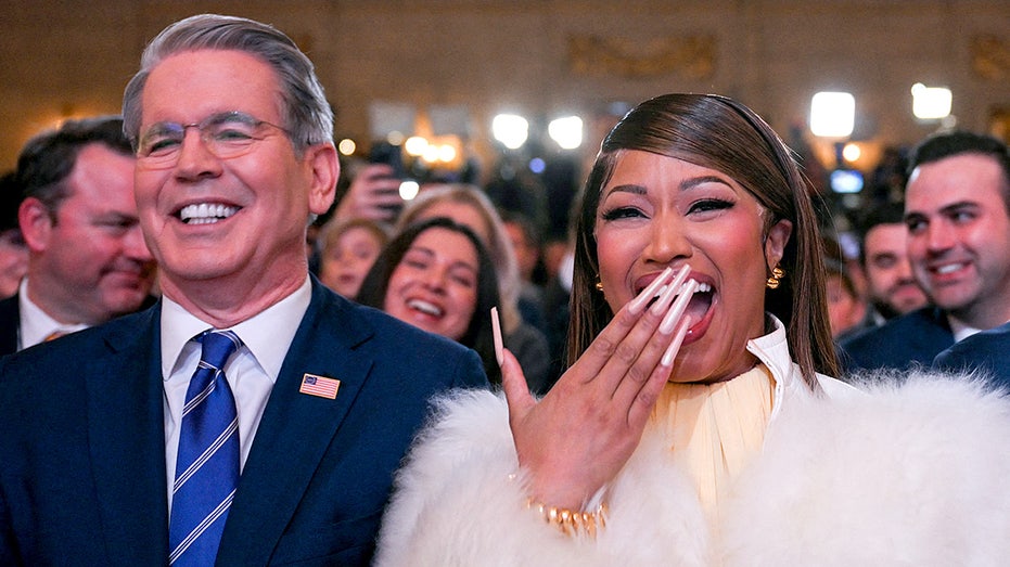 يقف سكوت بيسنت ونيكي ميناج للاستماع بينما يتحدث دونالد ترامب على المنصة خلال حدث ما.