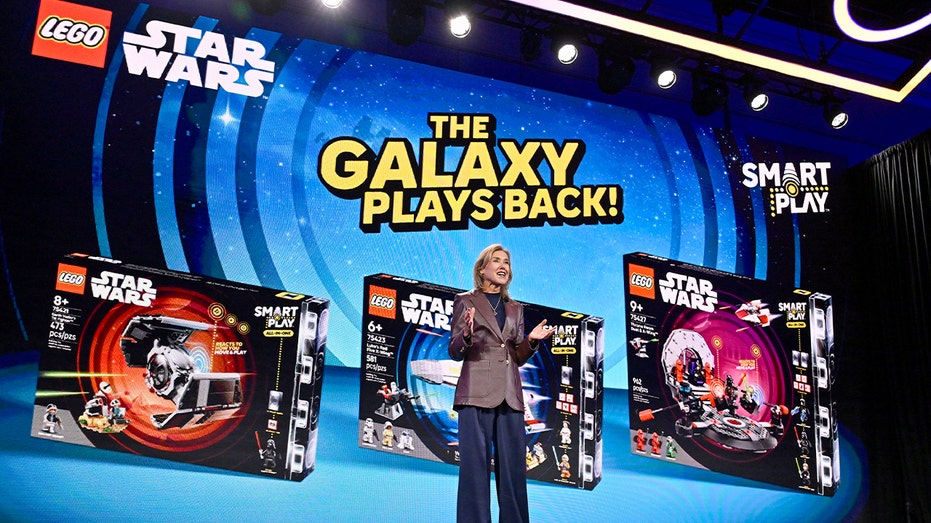 أحد المسؤولين التنفيذيين في LEGO يخاطب الجمهور من منصة المؤتمر تحت إضاءة الحدث الساطعة.