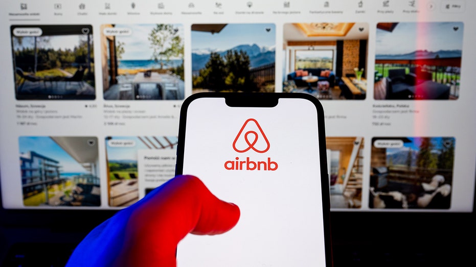 يتم عرض شعار Airbnb على الهاتف الذكي أمام قوائم العقارات.
