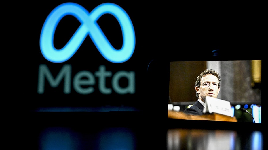 هاتف ذكي يعرض صورة مارك زوكربيرج معروض أمام شاشة الكمبيوتر وعليه شعار Meta.