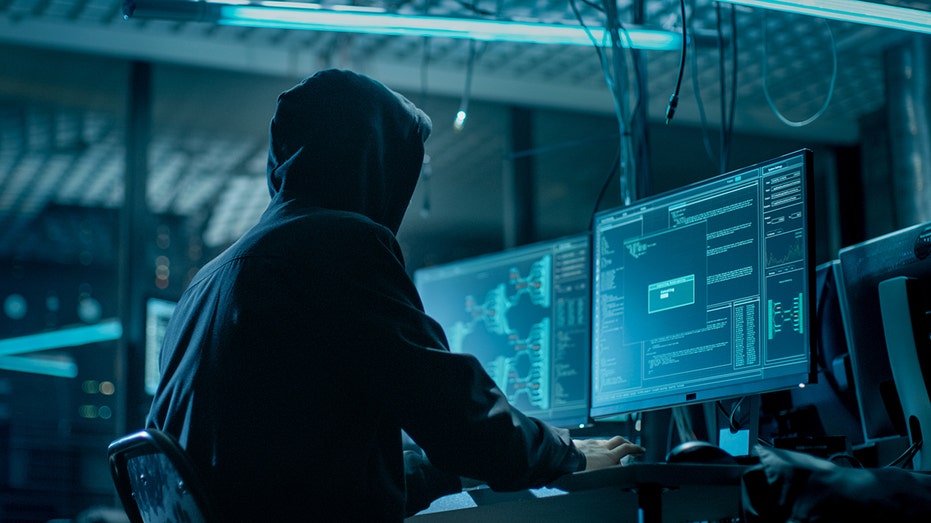 لقطة من الخلف لقراصنة مقنعين يقتحمون خوادم بيانات الشركة من مخبأه تحت الأرض. يتمتع المكان بجو مظلم وشاشات عرض متعددة وكابلات في كل مكان.